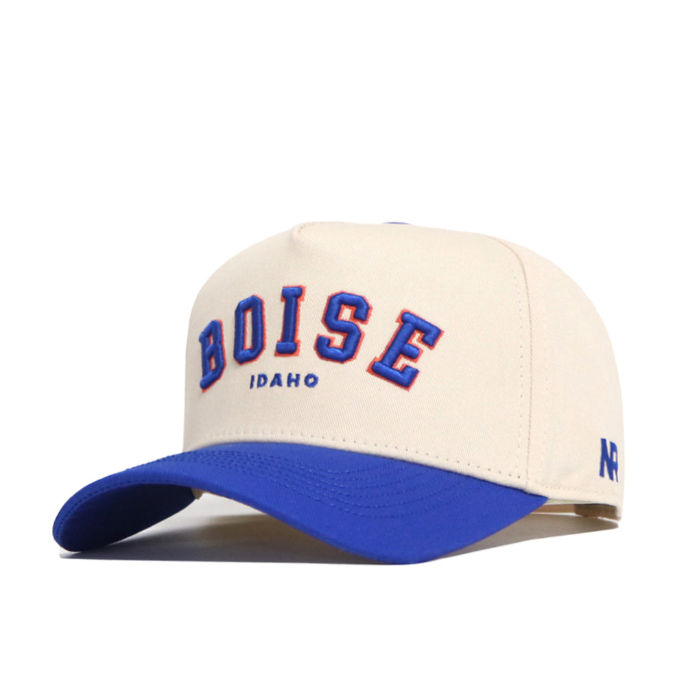 The Boise Hometown Hat by No Rivals is a cream cotton baseball cap with BOISE and IDAHO embroidered in blue and orange on the front, a blue brim, structured fit, and NP stitched in blue on the side.