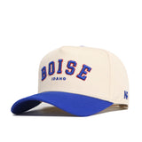 The Boise Hometown Hat by No Rivals is a cream cotton baseball cap with BOISE and IDAHO embroidered in blue and orange on the front, a blue brim, structured fit, and NP stitched in blue on the side.