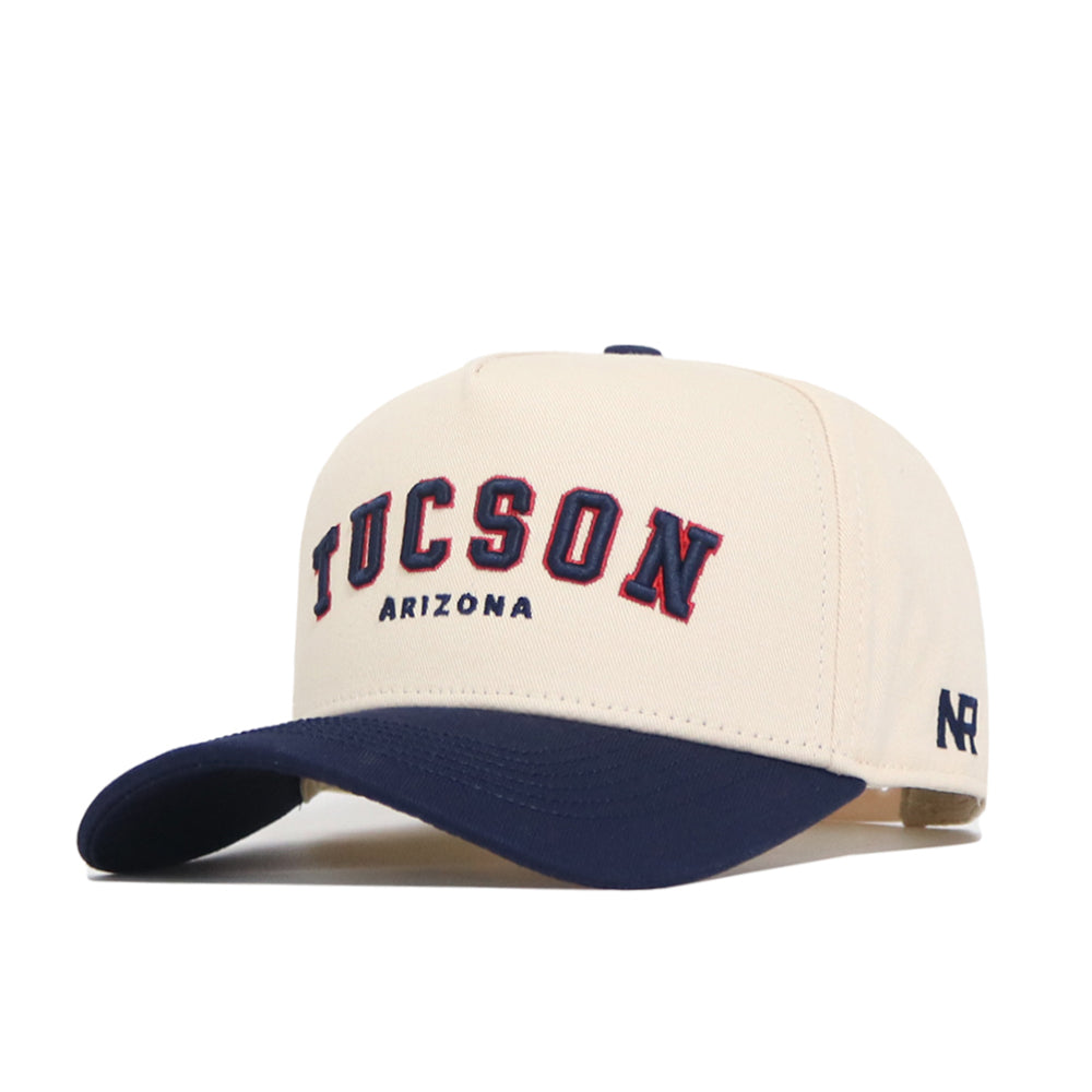 The No Rivals Tucson Hometown Hat is a beige cotton baseball cap with a dark blue brim, featuring "TUCSON" in bold blue and red above "ARIZONA" and "NR" stitched on the side for a structured, classic look.