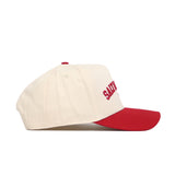 The Salt Lake City Hometown Hat by No Rivals is a cream cotton baseball cap with a red curved brim and red "SAINT" embroidery on the side, shown in side profile against a white background.