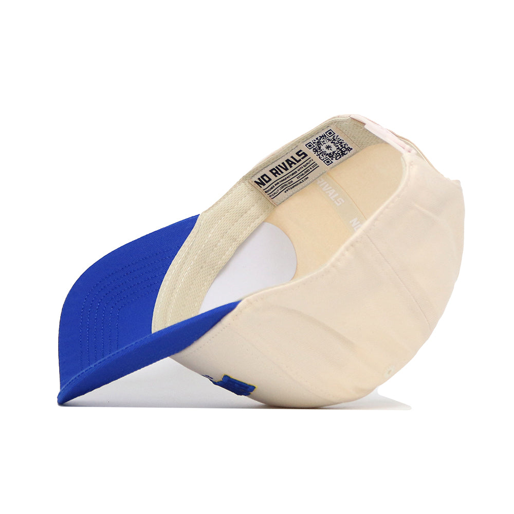 The Brookings Hometown Hat by No Rivals features a cream cotton body and blue brim, with an inside label reading NO RIVALS. The snapback cap is shown upside down on a plain white surface.