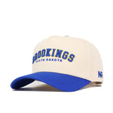 The Brookings Hometown Hat by No Rivals features a cream structured fit with a blue bill, high quality cotton, "BROOKINGS SOUTH DAKOTA" embroidered in blue/yellow on the front, "NR" on the side, and an adjustable snapback closure.