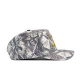 A side view of the No Rivals Oregon Outland Hat, a flat-brimmed snapback baseball cap with a camouflage pattern and a small yellow embroidered logo on the front, made from high-quality cotton, shown on a white background.