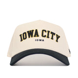 The Iowa City Hometown Hat by No Rivals features a structured white fit, a black curved brim, "IOWA CITY" in large yellow-outlined black letters, and "IOWA" in smaller blue letters on the front, crafted from high quality cotton.