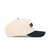 The No Rivals Iowa City Hometown Hat is a beige snapback with a black brim, shown from the side. It features raised black and yellow embroidery on the front, a structured fit, and an eyelet for ventilation.