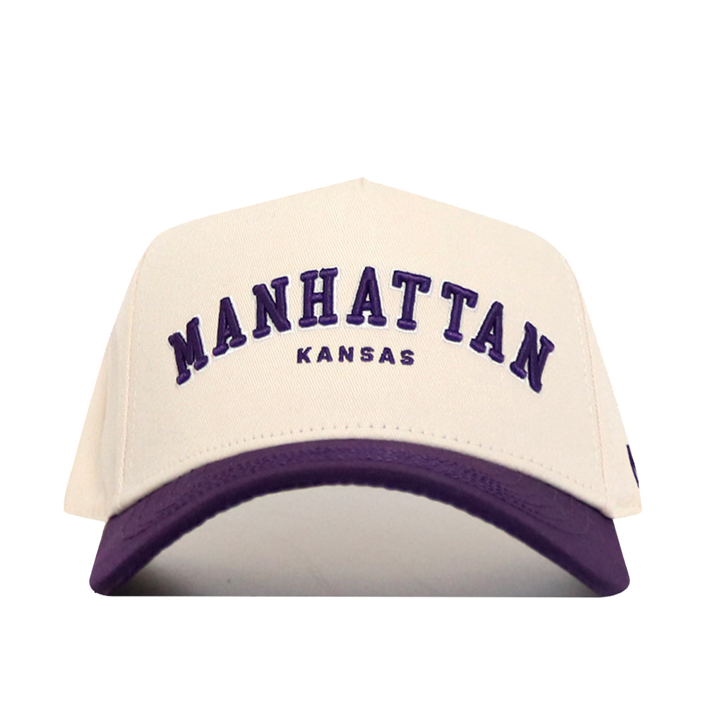 The No Rivals Manhattan Hometown Hat is a cream cotton baseball cap featuring "MANHATTAN KANSAS" embroidered in purple, a matching purple brim, and an adjustable snap back for comfort.