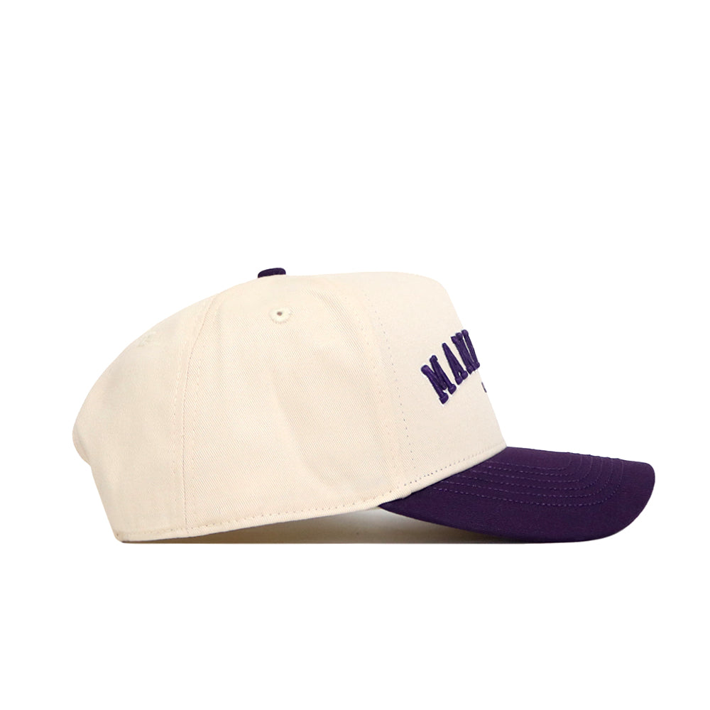 The No Rivals Manhattan Hometown Hat is a cream baseball cap with a dark purple brim, side view. Made from high-quality cotton, it features purple embroidery on the front and a structured fit for enhanced style.
