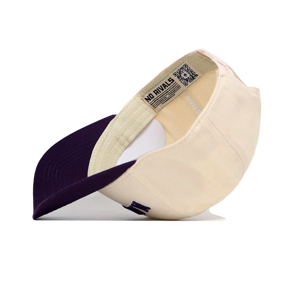 The No Rivals Manhattan Hometown Hat features a cream crown and dark purple brim, shown upside down to display the inside label, detailed stitching, and snapback adjustment for a structured fit.