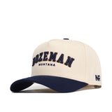 The No Rivals Bozeman Hometown Hat is a cream cap with a navy brim, structured fit, soft cotton, "BOZEMAN MONTANA" embroidered in navy and gold, "NR" on the left, and an adjustable snapback closure.