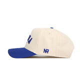 Side view of the Omaha Hometown Hat by No Rivals, a cream-colored structured cotton cap with a blue brim. Blue embroidery accents the front and “NR” is stitched on the side, showcasing classic baseball styling.