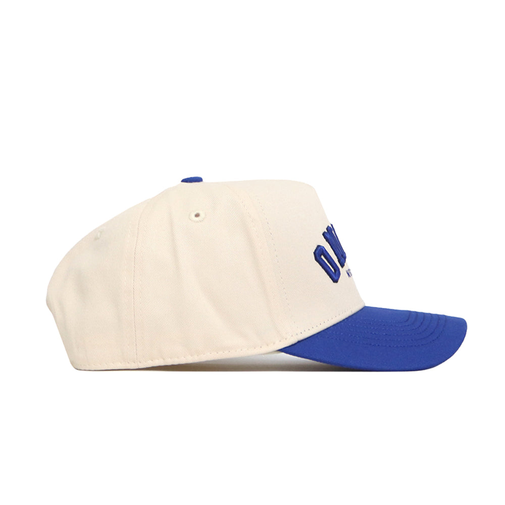 The No Rivals Omaha Hometown Hat features cream-colored high-quality cotton, a royal blue brim and top button, bold raised blue lettering on the front, and a structured fit for style and comfort.