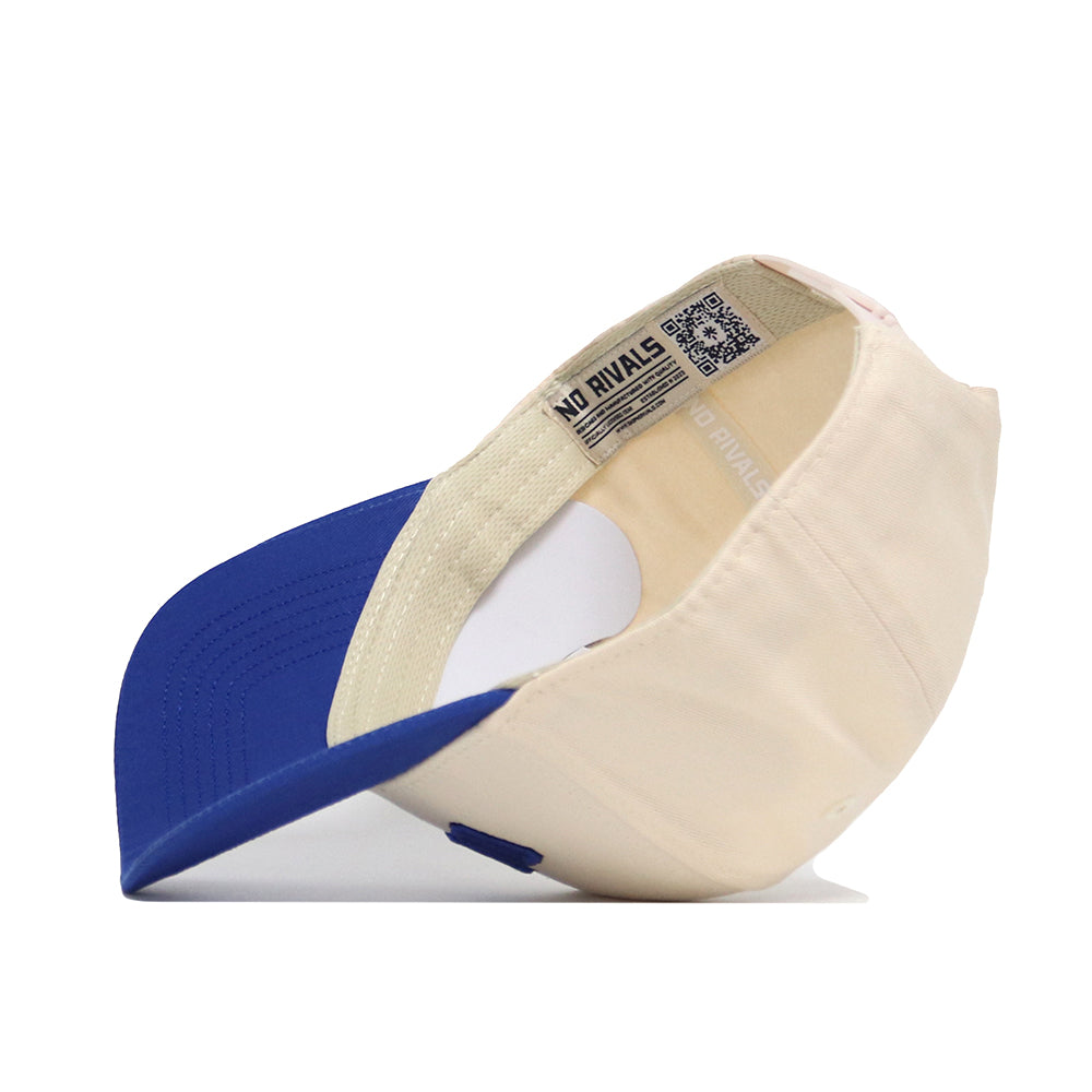 The Omaha Hometown Hat by No Rivals is shown upside down, displaying its inside tags and adjustable strap. This snapback hat features a blue bill with beige panels for a comfortable, stylish look.