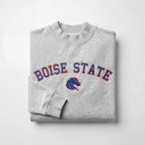 The Boise State Mock Neck by No Rivals is a folded gray sweatshirt with a mock neck, featuring blue and orange BOISE STATE lettering and a Bronco logo, plus “NO RIVALS” in white on the sleeve. Displayed against a plain white background.