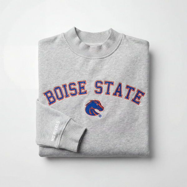 The Boise State Mock Neck by No Rivals is a folded gray sweatshirt with a mock neck, featuring blue and orange BOISE STATE lettering and a Bronco logo, plus “NO RIVALS” in white on the sleeve. Displayed against a plain white background.