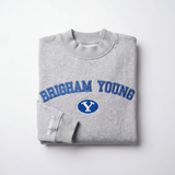 The BYU Mock Neck by No Rivals is a folded gray heavyweight cotton sweatshirt featuring "Brigham Young" in blue letters and a white Y in a blue oval on the chest, with "NO RIVALS" in small white letters on the sleeve.