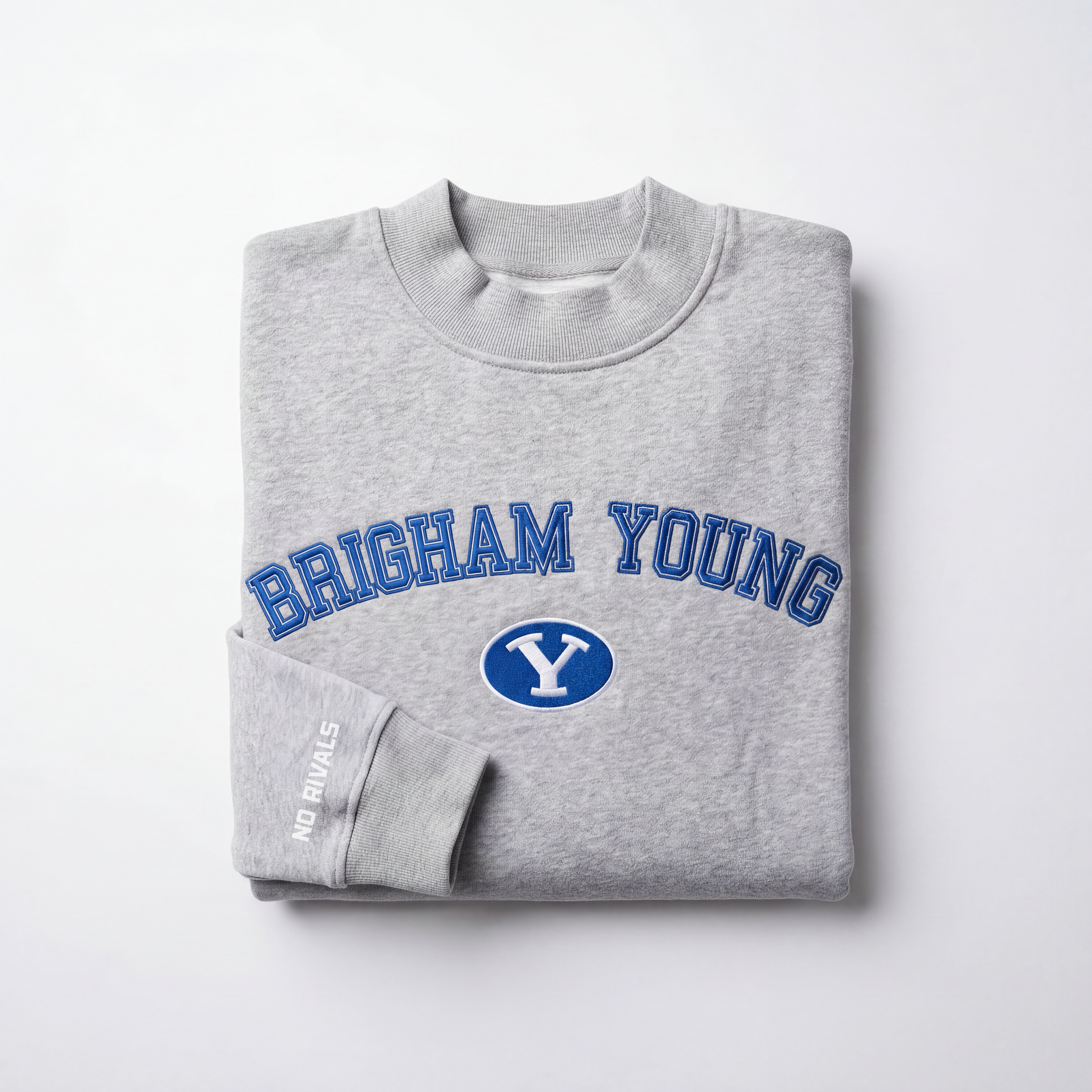 The BYU Mock Neck by No Rivals is a folded gray heavyweight cotton sweatshirt featuring "Brigham Young" in blue letters and a white Y in a blue oval on the chest, with "NO RIVALS" in small white letters on the sleeve.