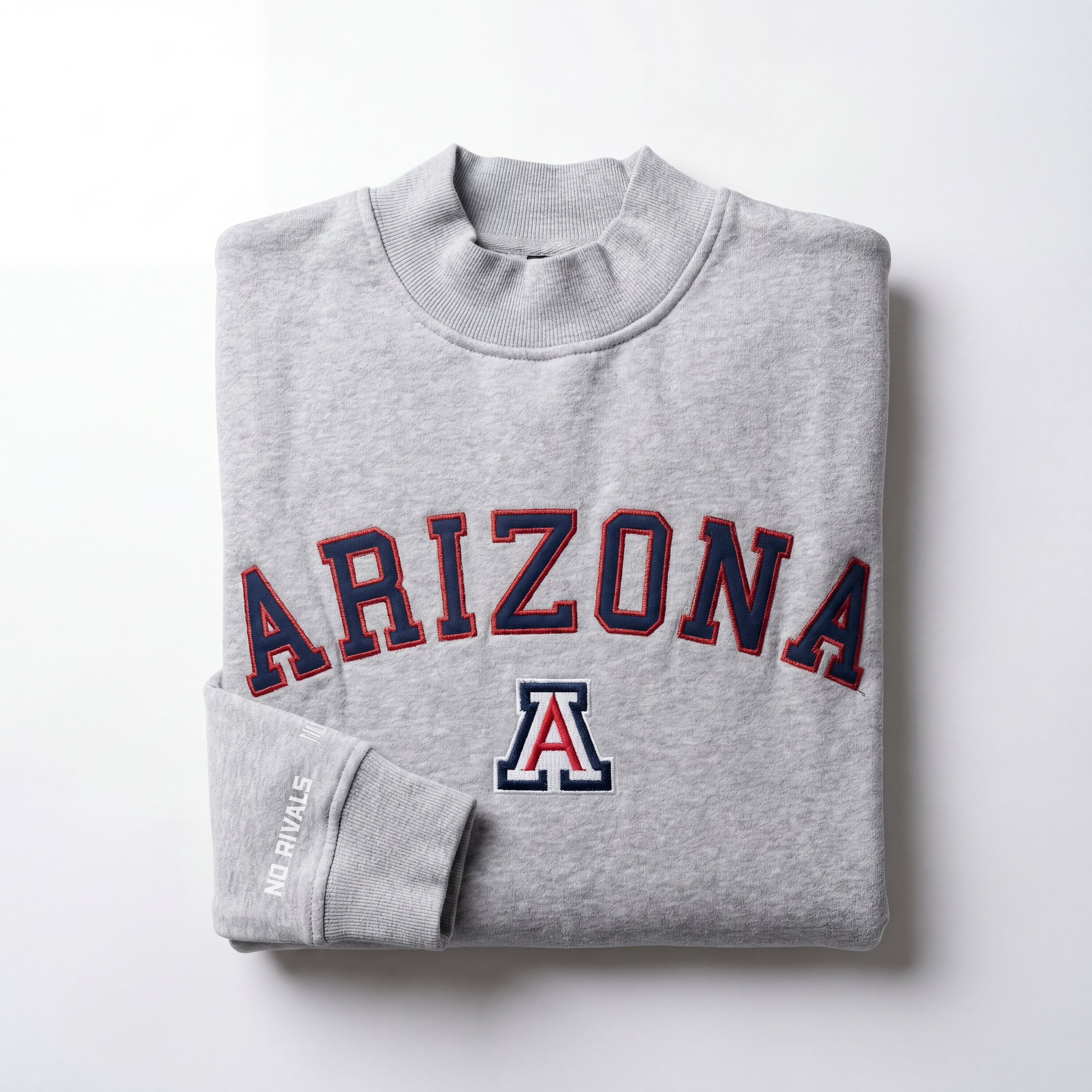 The No Rivals Arizona Mock Neck is a folded grey, oversized sweatshirt with "ARIZONA" in bold red and blue, a University of Arizona logo underneath, and "NO RIVALS" in small white text on the left sleeve.