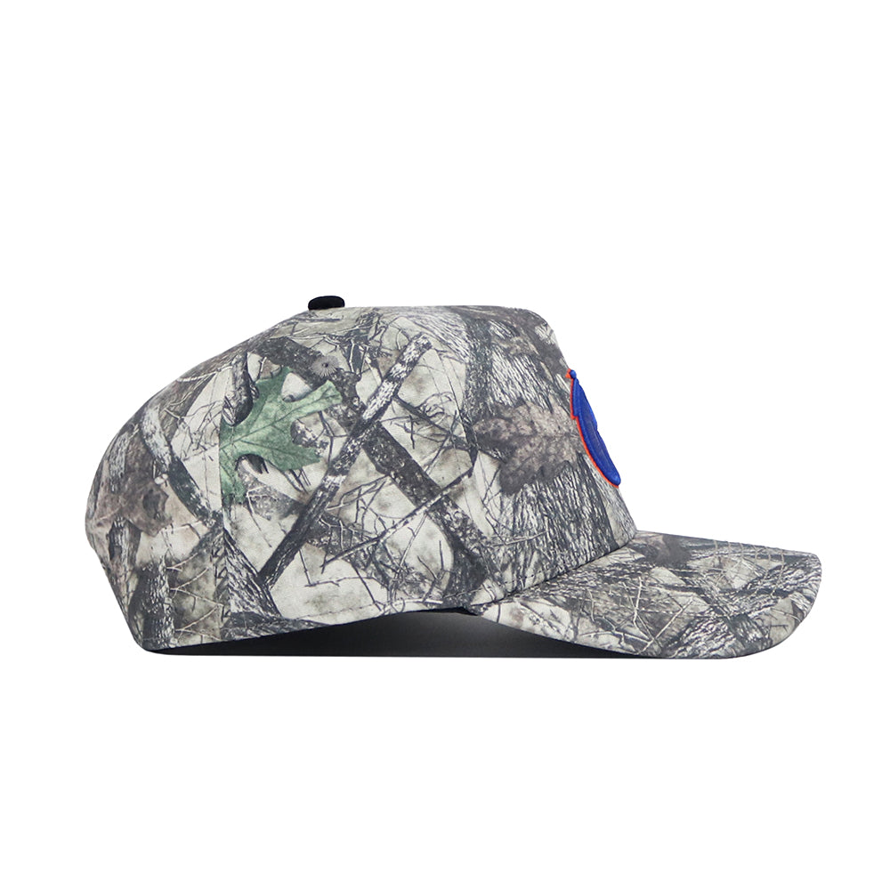 The Boise State Outland Hat by No Rivals is a camouflage snapback cap made of high-quality cotton, seen in side profile on a white background. A blue circular patch with red trim accents the structured front for a classic look.