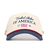 The No Rivals USA Classic Americana Hat is a beige snapback featuring "United States OF AMERICA 1776" in blue, a small U.S. flag, and a blue bill with red trim, made from high-quality cotton for a structured fit.