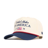 The No Rivals USA Classic Americana Hat features cream cotton, "United States of America 1776" in navy embroidery, a small American flag patch, a navy curved brim with red trim, and offers a structured snap back fit.