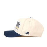 The No Rivals WVU Mountaineers Stacked Mascot Hat features a cream-colored crown with a navy blue brim, a yellow and navy embroidered logo on the front, and “NR” stitched on the side. Made from performance fabric, it has a classic snap back closure and is displayed against a white background.