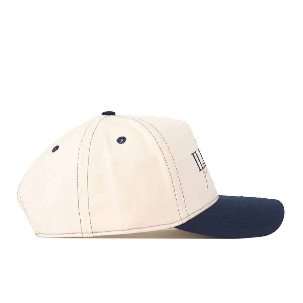 A side view of the No Rivals Illinois Fighting Illini Vintage Hat, featuring a cream-colored crown and a dark blue brim. Made from high quality cotton, this snapback cap displays visible stitching and two small ventilation holes on the side.