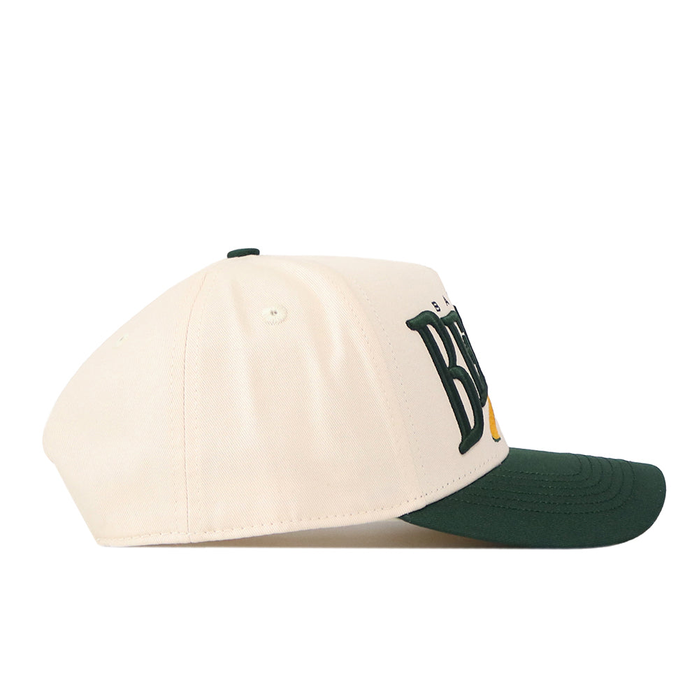 The Baylor Bears Stride Hat by No Rivals is a cream-colored baseball cap with a green brim and dark green embroidered lettering partially visible on the front, featuring a snapback closure. The hat is shown from the side against a white background.