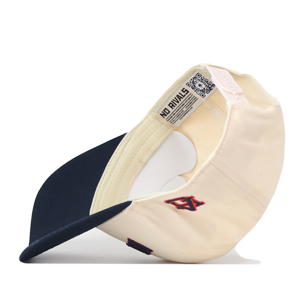 The Right Side Up Auburn Hat - Classic Colors by No Rivals is shown upside down to reveal the inside label with “NO RIVALS” and a QR code. Designed for your Gameday Fit, this beige and navy cap features an embroidered logo, a contrasting dark brim, and an adjustable snap back for all-day comfort.