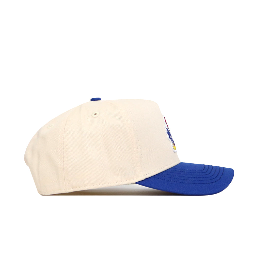 The No Rivals Kansas Logo Patch Hat, a cream-colored cotton blend baseball cap with a blue brim and patch embroidery, is shown from the side on a white background.