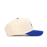 The No Rivals Kansas Logo Patch Hat, a cream-colored cotton blend baseball cap with a blue brim and patch embroidery, is shown from the side on a white background.