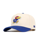 The No Rivals Kansas Logo Patch Hat is a beige cotton-blend snapback with a blue brim, featuring the University of Kansas Jayhawk logo patch on the front and "NR" embroidered on the side.