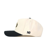 The Classic Colorado Buffs Hat is a cream snapback with a black brim, made from high-quality cotton. It features a small black NR embroidered on the side and a partially visible circular logo on the front for a structured fit.