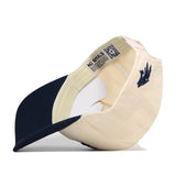 A No Rivals Nevada Wolf Pack Stadium Hat in cream and navy, turned inside out to display the inner label featuring text and a QR code, along with a paper insert and an officially licensed navy blue emblem stitched on the side—perfect for highlighting both its premium quality and unique embroidered logos.