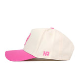 The EWU Pink Out Hat by No Rivals is a cream-colored baseball cap with a pink bill and pink embroidered details, including “NR” on the side. Made from performance fabric, the hat showcases an embroidered logo and is displayed in a side view against a white background.