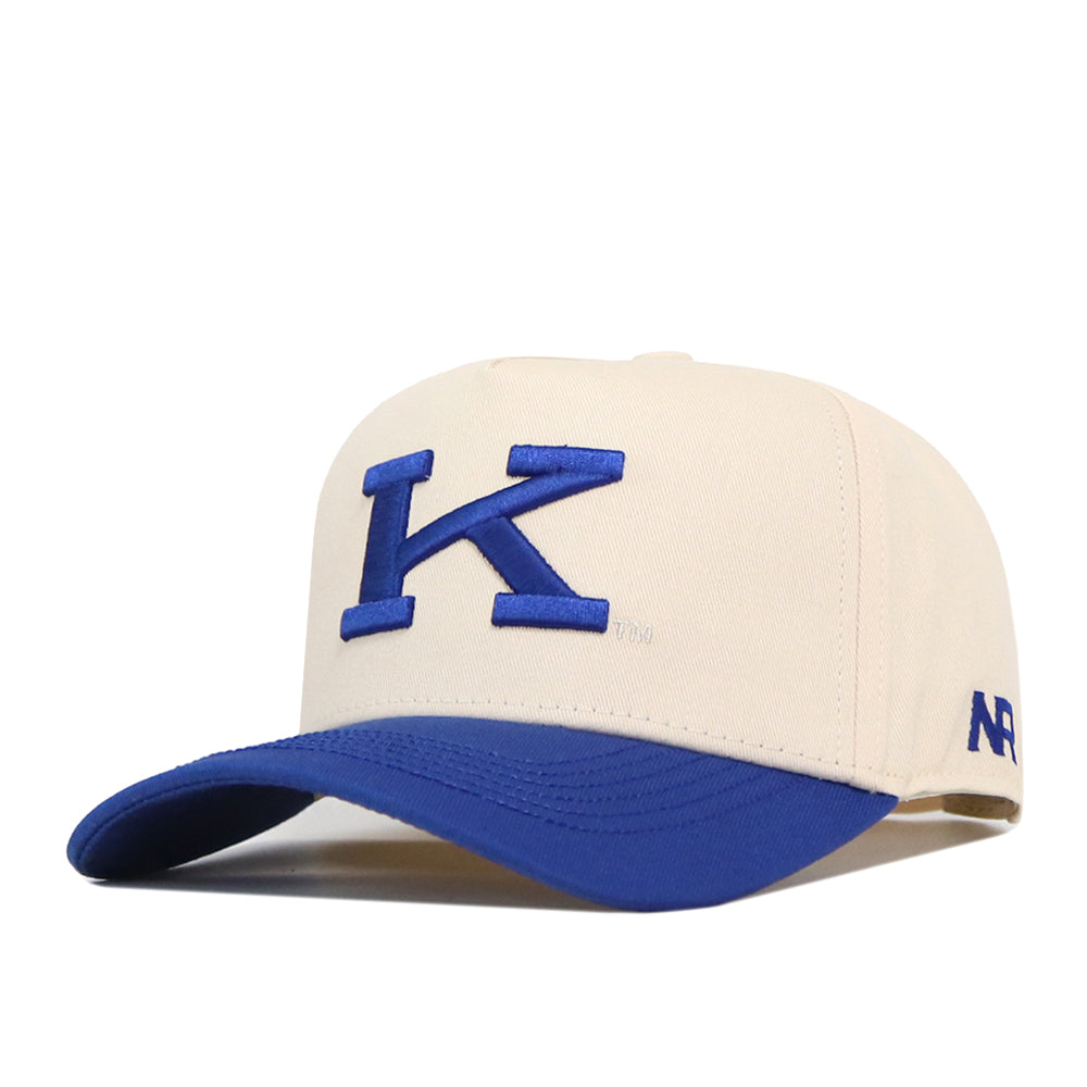 The Kentucky Vintage K Hat - Classic by No Rivals is a cream-colored snapback featuring a blue embroidered “K” logo on the front and a blue curved brim. The side is detailed with ‘47’ stitched in blue, making it the perfect addition to your gameday fit.