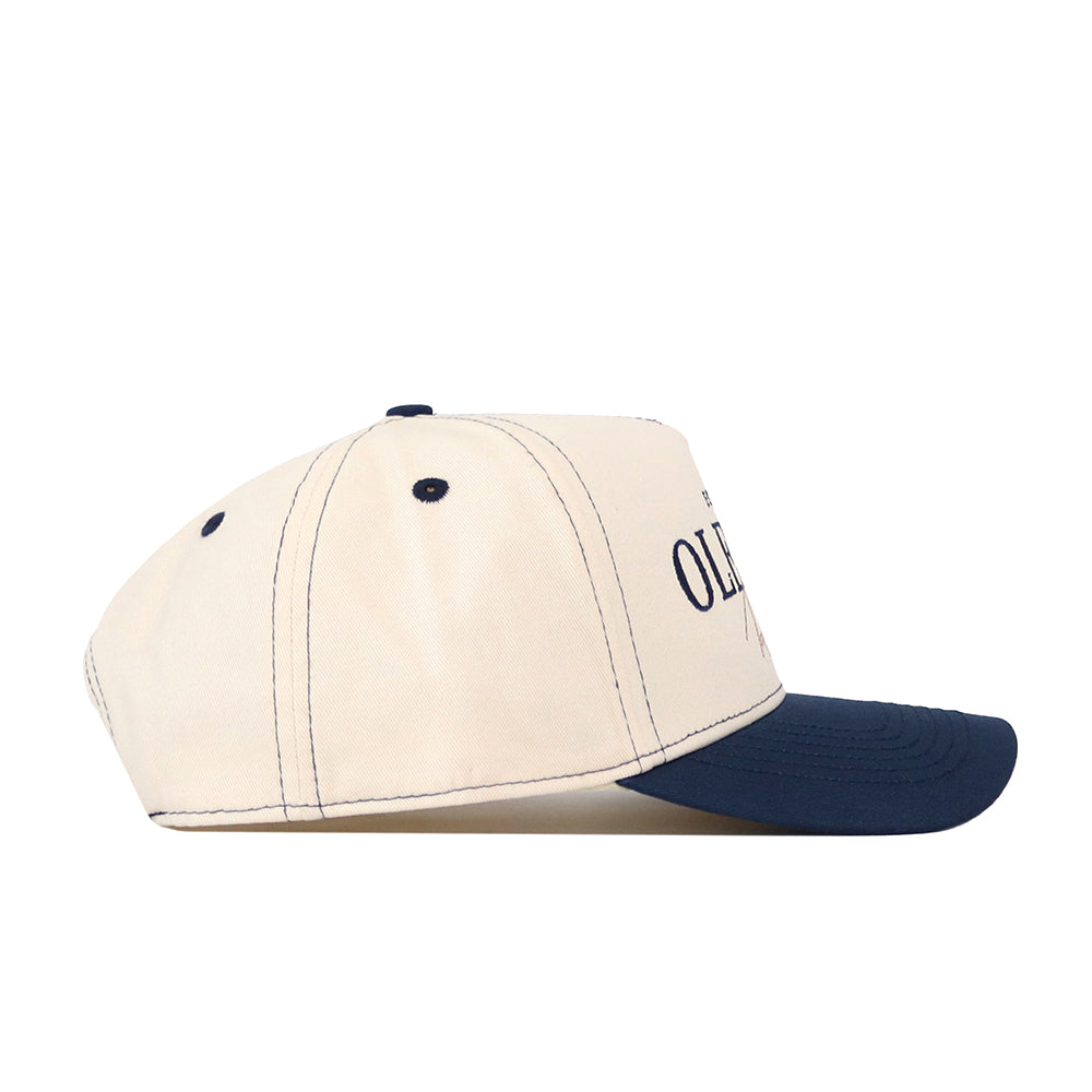 Showcase your team spirit with the No Rivals Ole Miss Rebels Vintage Hat – Navy. This baseball cap features a cream-colored crown and a navy blue brim, shown from the side. Designed with dark stitching details, visible ventilation eyelets, and an easy-to-adjust snap back closure, it ensures all-day comfort. Part of the front panel text is visible, making this hat the perfect finishing touch to your gameday outfit.