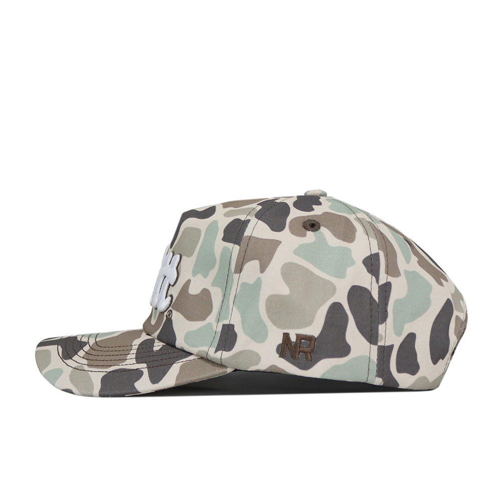 The Pittsburgh Panthers Huntsman Hat by No Rivals is a camouflage-patterned snapback with white embroidered letters on the front and brown NR initials stitched on the side, viewed from the left. This hat features a structured fit and is crafted from durable cotton material.