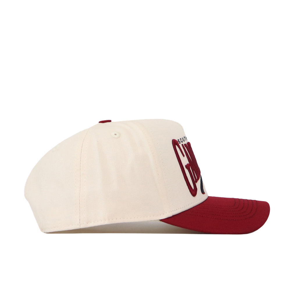 The No Rivals South Carolina Gamecocks Stride Hat features a cream-colored crown with a maroon brim and matching maroon button on top. Bold maroon text is displayed prominently on the front panel. Made from high quality cotton for lasting comfort and durability, this structured-fit cap is pictured from the side against a white background.