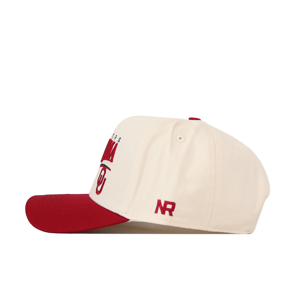 The No Rivals Oklahoma Sooners Stride Hat is a cream-colored snapback baseball cap with a red bill, red top button, and red embroidered accents. Made from soft cotton, this structured-fit hat showcases the NR logo and partial lettering on the side.