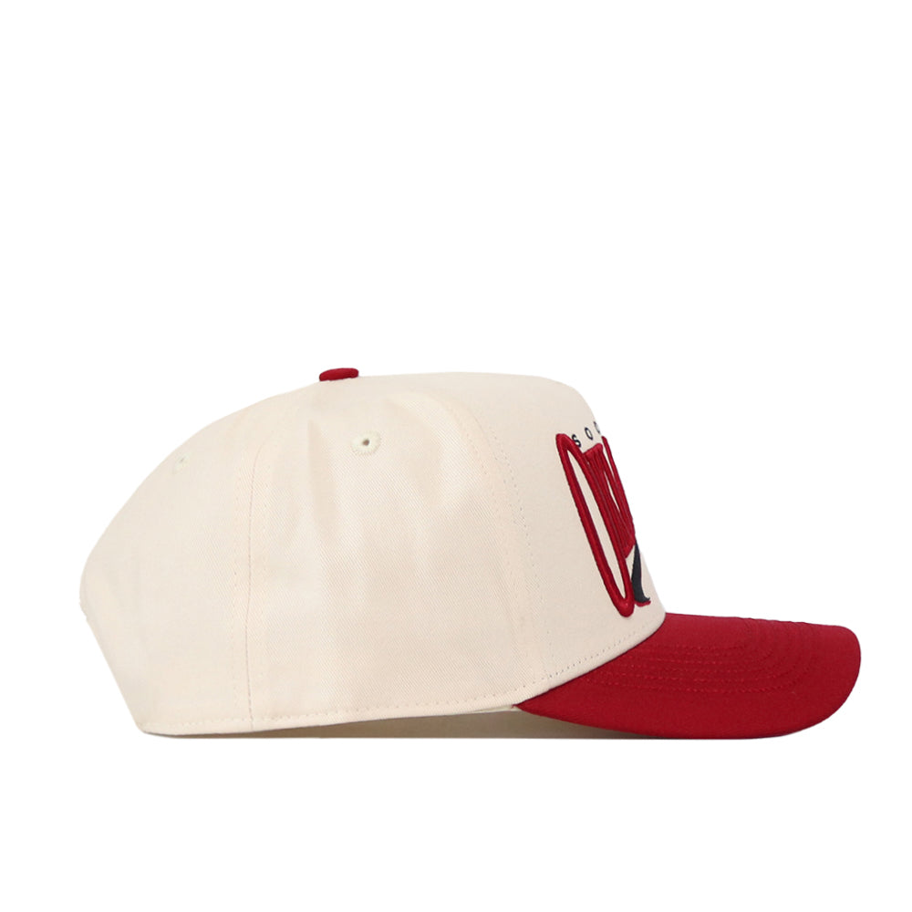 The Oklahoma Sooners Stride Hat by No Rivals is a cream-colored cotton baseball cap with a structured fit, featuring a red brim and red embroidered lettering on the front. It is displayed in a side profile view against a white background.