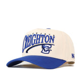 The No Rivals Creighton Bluejays Stride Hat is a cream and blue snapback cap featuring “Creighton Bluejays” text and an embroidered blue jay mascot logo on the front, officially licensed for authentic team pride.