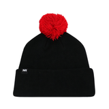 The Nebraska Cornhuskers Patch Beanie by No Rivals is a black knit beanie featuring a large red pom-pom on top and a small tag with the embroidered letters NR on the folded brim, crafted from high-quality cotton for a comfortable gameday fit.