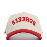 The Upside Down Scheels Hat is a white cotton baseball cap with a red brim, red upside-down embroidered SCHEELS lettering on the front, and an adjustable snap back closure.