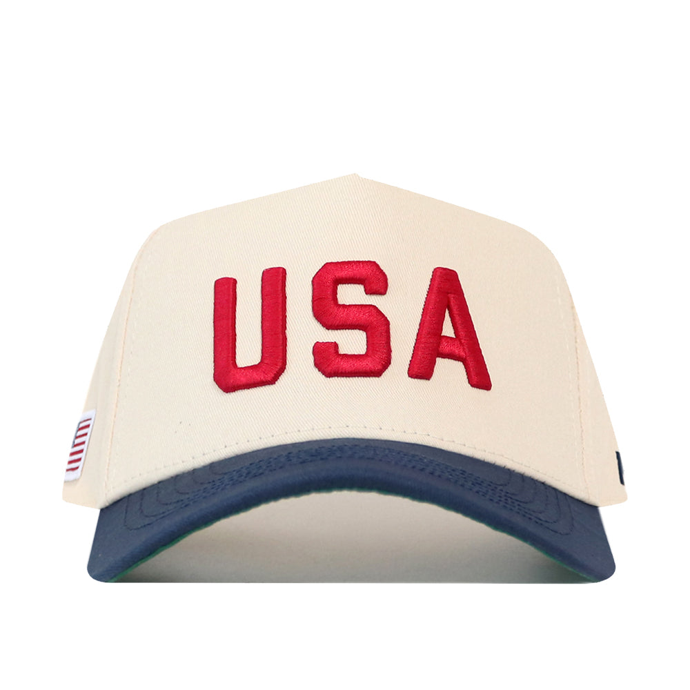 No Rivals USA Vintage Hat - 5 Panel Structured in cream with a dark blue brim, featuring red USA embroidery and a small American flag tag on the side.