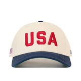 USA Vintage Hat - 6 Panel Structured in off-white cotton with USA embroidered in red letters, a navy blue brim, and a small American flag patch on the side.