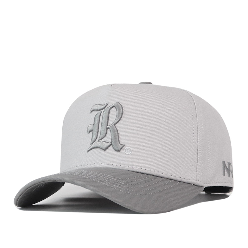 A light gray Rice Graphite Hat by No Rivals, featuring a dark gray brim and an Old English style letter R embroidered on the front.