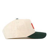 Side profile of a cream-colored No Rivals Miami Halftime Hat with a dark green brim and a small red rectangular patch on the side.