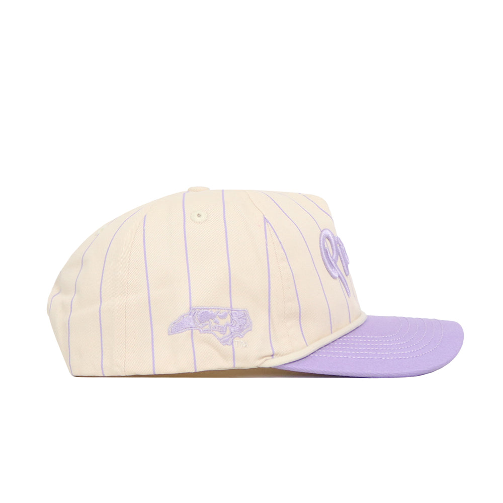 The No Rivals ECU Powder Purple Pinstripe Hat is a cream snapback with thin lavender stripes and a lavender brim, crafted from premium cotton. It features an embroidered lavender graphic on the side and a partial script logo on the front.