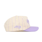 The No Rivals ECU Powder Purple Pinstripe Hat is a cream snapback with thin lavender stripes and a lavender brim, crafted from premium cotton. It features an embroidered lavender graphic on the side and a partial script logo on the front.
