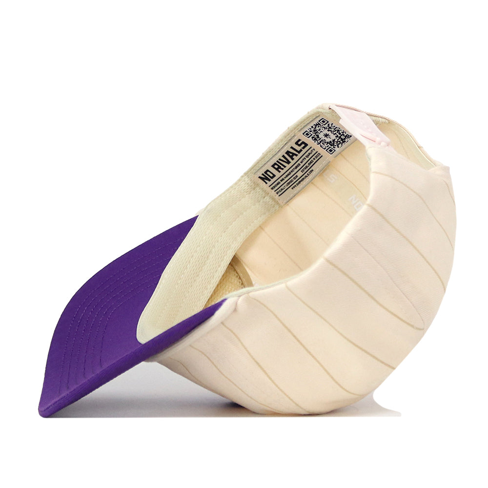 A Washington Pinstripe Hat by No Rivals is flipped upside down, exposing its inner lining with a label reading NO RIVALS and a black and white QR code. The purple and cream snapback cap features an embroidered logo, adding a stylish touch to this officially licensed piece.